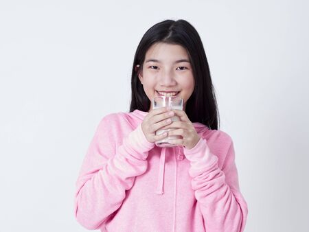 Portrait of cheerful girl with glass of milk while smiling at camera on white background.の写真素材