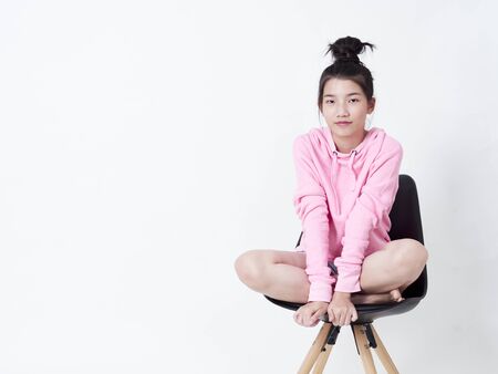 Portrait of cute girl wearing sweater hoodie pink while sitting black chair isolated on white background.の写真素材