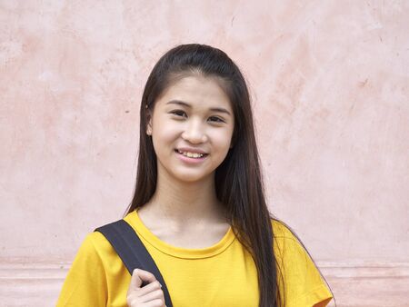 Portrait of cute student girl with backpacks smiling at camera while standing outdoors in the park.