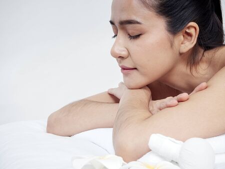 Beautiful woman and spa accessories, frangipani flowers, herbal compress ball on massage table white backgroundの写真素材