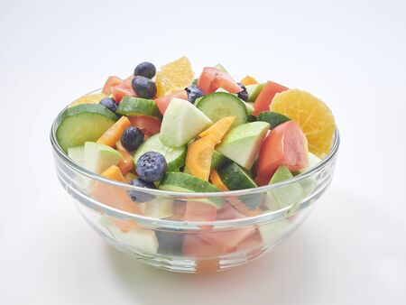 Mixed vegetable salad with fresh fruit in a glass bowl on a white background. carrot, orange, blueberry, Apple, lemon, tomato, cucumber. Healthy menu design. diet food. copy space, flat layの写真素材