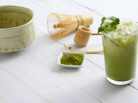 Iced Matcha Latte Tea and homemade tea brewing accessories with bamboo whisk, green tea powder on white wooden background.の写真素材