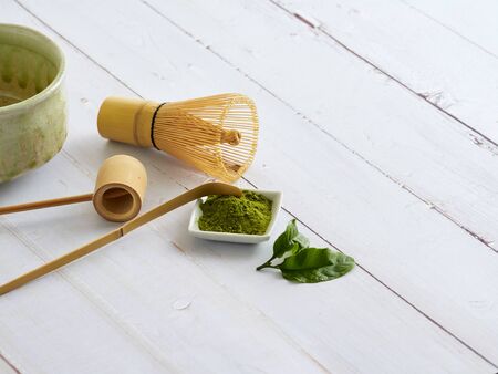 Traditional matcha green tea brewing with bamboo whisk, green tea powder on old white wooden table.
