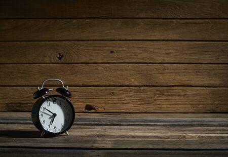 Black vintage alarm clock on wooden planks background in the dark.の写真素材