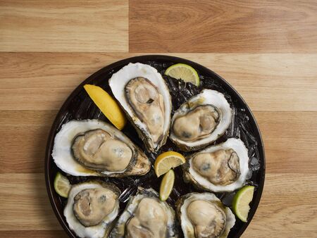Close-up of fresh opened oysters on ice and lemon in a tray on wooden background.