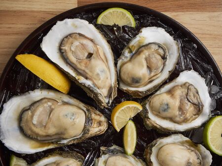 Close-up of fresh opened oysters on ice and lemon in a tray on wooden background.