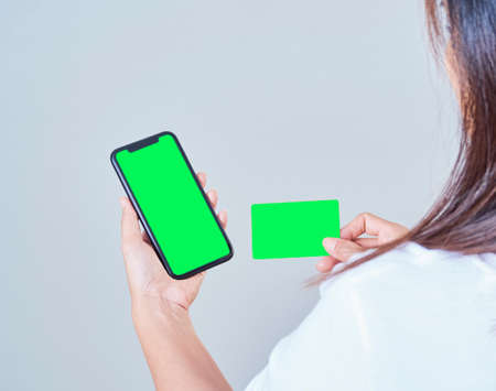 Mock-up image of woman hand holding mobile phone, blank screen and credit card on gray background