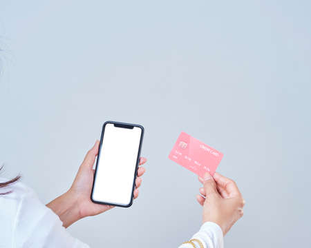 Woman with shopping bags and credit card while using smartphone to pay through banking app.