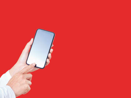 Close up of woman hand touching a smartphone white display isolated on red backgroundの写真素材