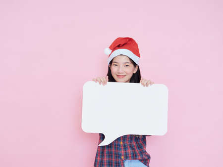 Cute teenage girl in santa hat holding white blank poster on pink background