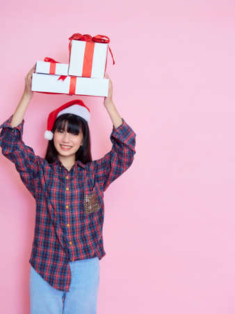 Cheerful young girl wearing santa hat with holding gift boxes on pink backgroundの写真素材