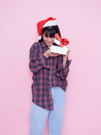 Happy girl in Santa hat opening a gift box against pink backgroundの写真素材