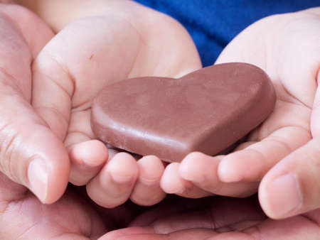 Woman and child holding heart-shaped chocolate. Close up