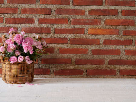 Roses in basket on wooden table against brick wall background. Space for text