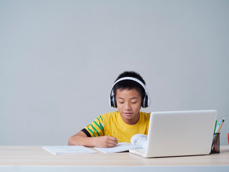 Little boy in headphones studying online using laptop. Social distance during quarantineの写真素材