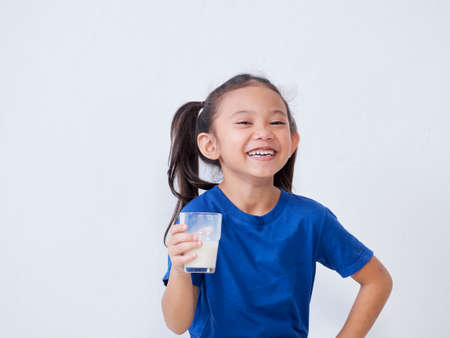 Portrait of happy little girl with glass of milk on light backgroundの写真素材