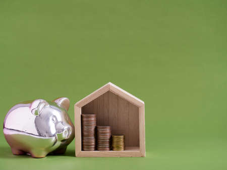 Piggy bank and house model with coins on green background. Space for textの写真素材