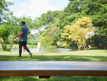 Blurred nature background. Empty wooden table in park with people sitting and relaxingの写真素材