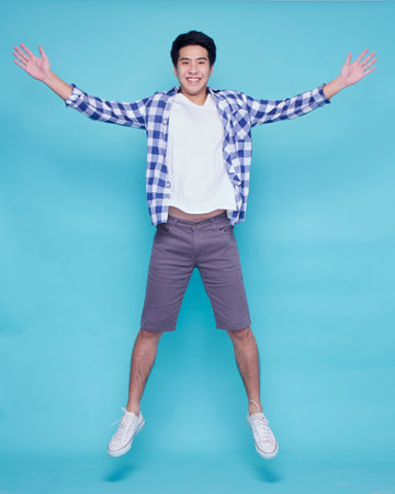 Portrait of young man jumping on blue background. Summer vacationの写真素材