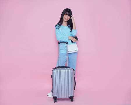 Young woman with suitcase and smartphone on pink background, space for text. Summer vacationの写真素材