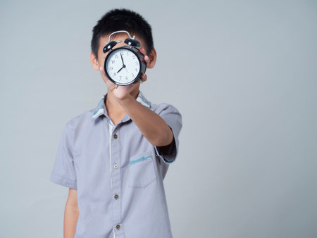 Little boy holding alarm clock on gray background