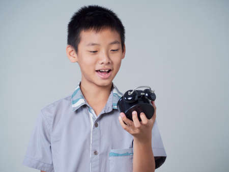 Little boy holding alarm clock on gray backgroundの写真素材