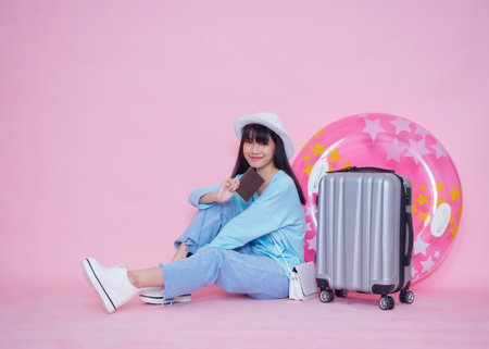 Beautiful woman with suitcase and passport for summer trip on pink background. Vacation travelの写真素材