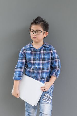 Asian boy ready to go to school and his hands hold the book against the gray wallの写真素材