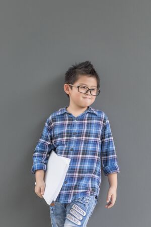 Asian boy feels excited when time to school and his hands hold the book against the wallの写真素材