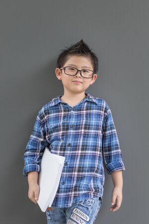Asian boy ready to go to school and his hands hold the white books against the the wallの写真素材