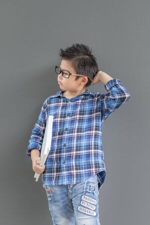 Little student boy feels nervous and thinking something, his hands hold the white books against the the wallの写真素材
