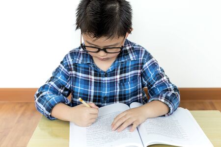 Little student boy in glasses doing his homework on the table with white backgroundの写真素材