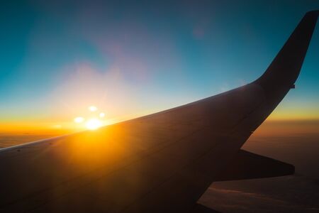 the wing of an airplane against the background of dawn high above the ground. thick clouds from the plane window blue Nemo with the rising sun and the wing of the planeの写真素材