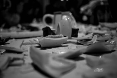 pieces of broken dishes on the table. pieces of broken clay and porcelain scattered on the table. parts of different dishes on a white background. broken plates cups and chaniki on the table. black and white photo picture background textureの写真素材