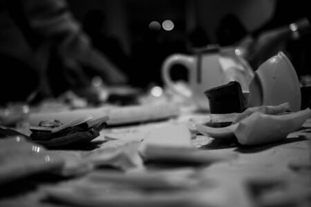 pieces of broken dishes on the table. pieces of broken clay and porcelain scattered on the table. parts of different dishes on a white background. broken plates cups and chaniki on the table. black and white photo picture background textureの写真素材