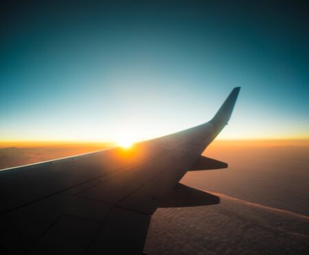 the wing of an airplane against the background of dawn high above the ground. thick clouds from the plane window blue Nemo with the rising sun and the wing of the planeの写真素材
