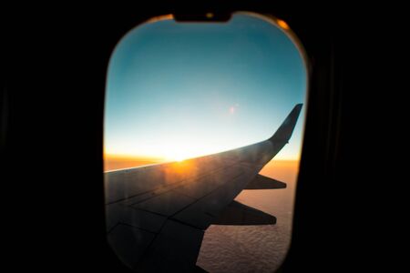 the wing of an airplane against the background of dawn high above the ground. thick clouds from the...