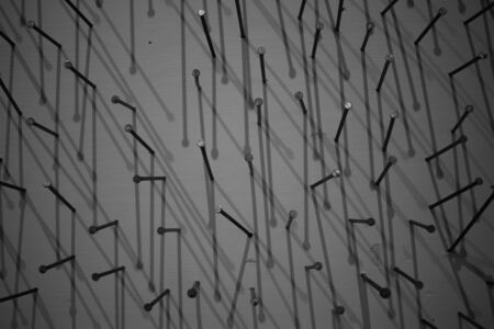 black and white photo of construction nails that are driven into the canvas and cast a shadow on it. macro photography of construction nails black construction nails on a white background nails casting a background on a white background. white painting with construction nails.の写真素材