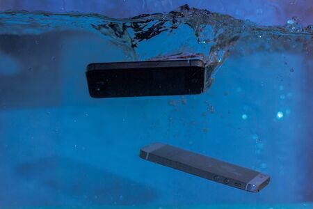 black and white phone dropped into the water. phone in water. blue water. phone in water...
