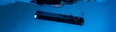 black and white phone dropped into the water. phone in water. blue water. phone in water bubbles.phone sinks in waterの写真素材