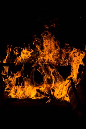 bright orange languages of a fire on wooden logs at night. wood on fire. bonfire at night. campfire. beautiful flame on black background. fire on black background. burning wood . beautiful fire texture. the texture of the campfireの写真素材