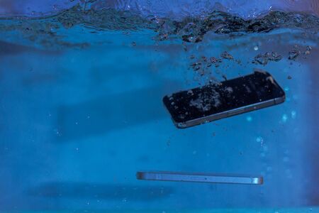 black and white phone dropped into the water. phone in water. blue water. phone in water...