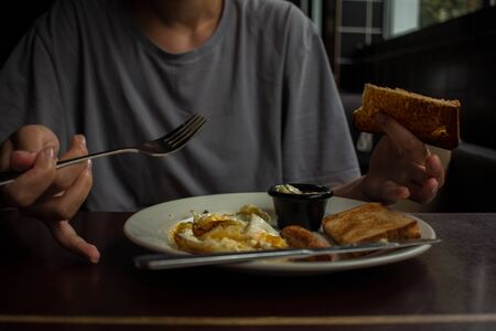 girl in gray t shirt eats scrambled eggs with toast sausage and cheeseの写真素材