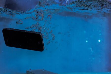 black and white phone dropped into the water. phone in water. blue water. phone in water...