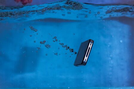 black and white phone dropped into the water. phone in water. blue water. phone in water bubbles.phone sinks in waterの写真素材