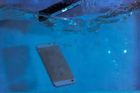 black and white phone dropped into the water. phone in water. blue water. phone in water bubbles.phone sinks in waterの写真素材