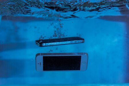 black and white phone dropped into the water. phone in water. blue water. phone in water bubbles.phone sinks in waterの写真素材