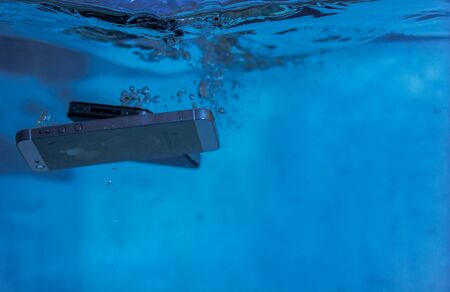 black and white phone dropped into the water. phone in water. blue water. phone in water bubbles.phone sinks in waterの写真素材