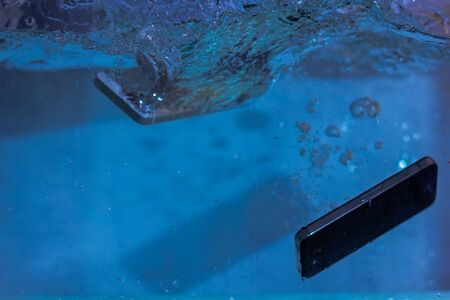 black and white phone dropped into the water. phone in water. blue water. phone in water bubbles.phone sinks in waterの写真素材