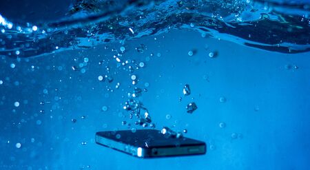 black and white phone dropped into the water. phone in water. blue water. phone in water bubbles.phone sinks in waterの写真素材